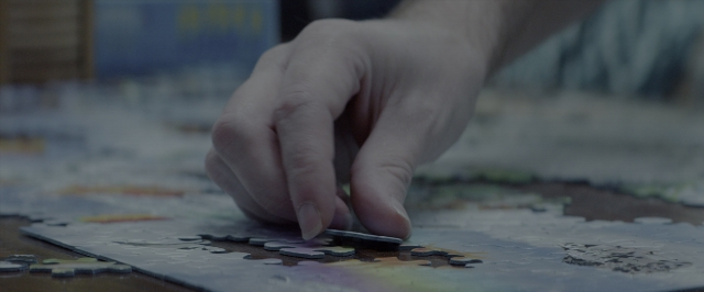 Wide shot frame from 10 Cloverfield Lane — room, table, hand
