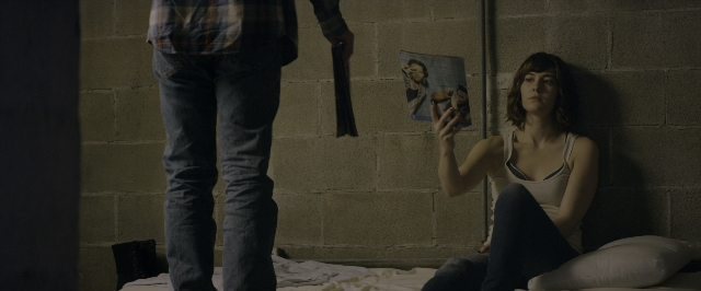 Wide shot frame from 10 Cloverfield Lane — sitting, book, standing