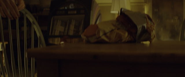 Wide shot frame from 10 Cloverfield Lane — book, room, table