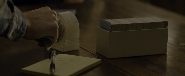 Wide shot frame from 10 Cloverfield Lane — sitting, room, table