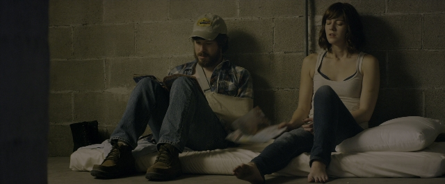 Wide shot frame from 10 Cloverfield Lane — sitting, book, room