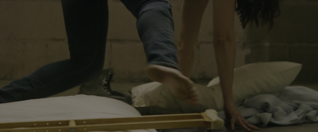 Wide shot frame from 10 Cloverfield Lane — room, bed, hand