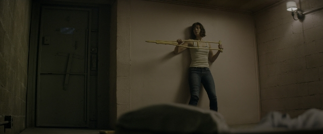 Close-up frame from 10 Cloverfield Lane — standing, room, bed