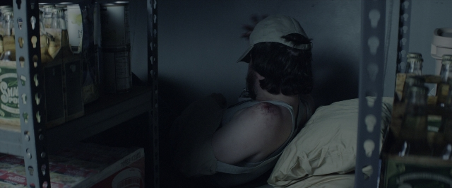 Wide shot frame from 10 Cloverfield Lane — room, bed, hat