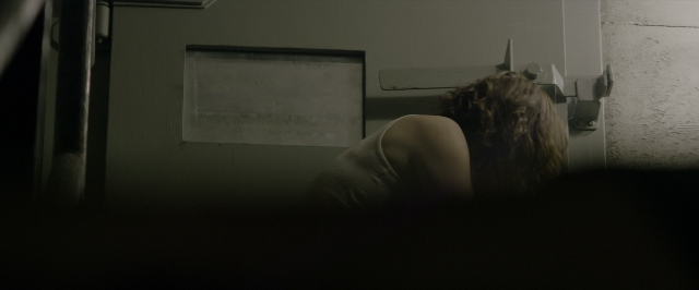 Wide shot frame from 10 Cloverfield Lane — bed, door, face