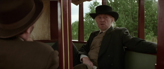 Wide shot frame from Unforgiven — sitting, hat, car