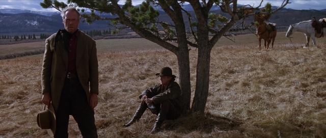 Wide shot frame from Unforgiven — sitting, standing, hat