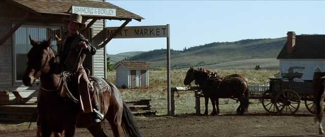 Wide shot frame from Unforgiven — sitting, hat, coat