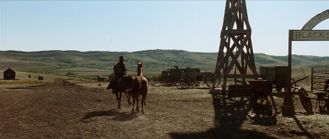 Wide shot frame from Unforgiven — sitting, walking, hat