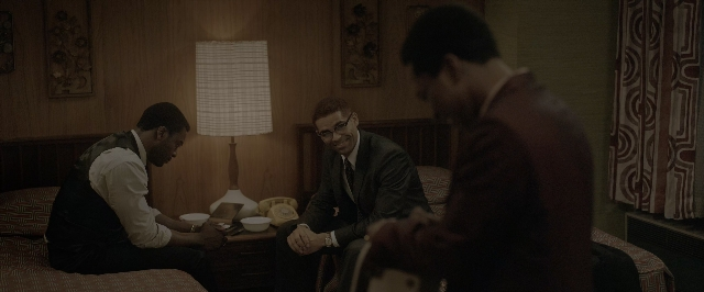 Wide shot frame from One Night in Miami — sitting, book, room