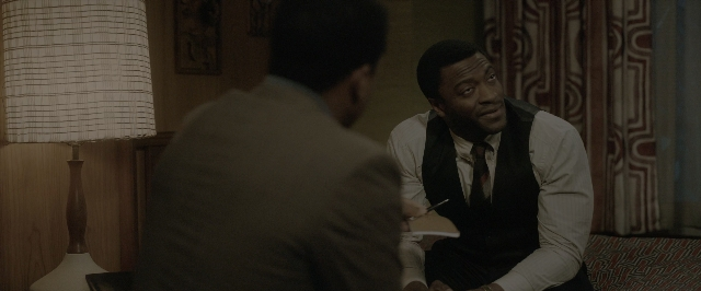 Wide shot frame from One Night in Miami — sitting, book, room