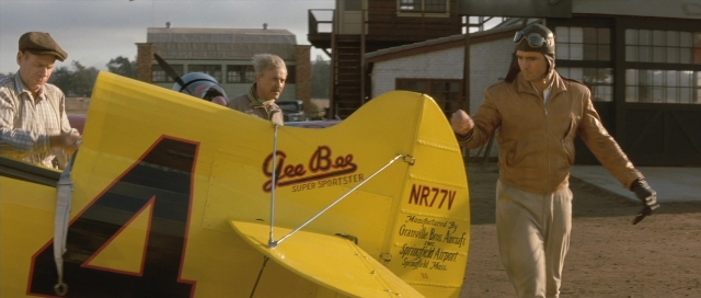 Medium shot frame from The Rocketeer — standing, hat, airplane