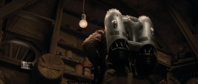Wide shot frame from The Rocketeer — standing, hat, wheel