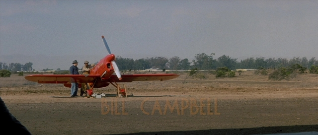 Wide shot frame from The Rocketeer — standing, hat, airplane