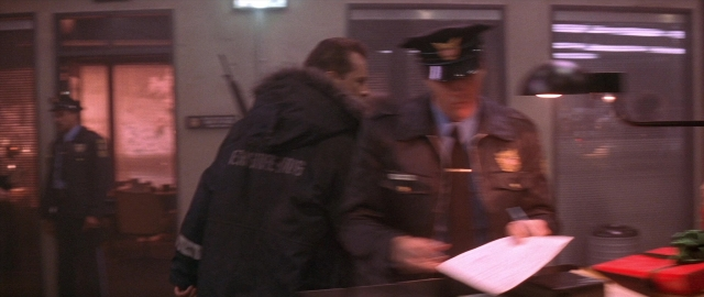 Wide shot frame from Die Hard 2 — standing, room, hat