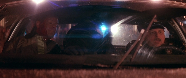 Wide shot frame from Die Hard 2 — sitting, street, hat