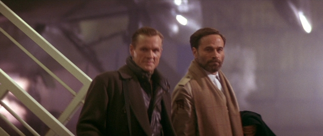 Wide shot frame from Die Hard 2 — standing, room, coat