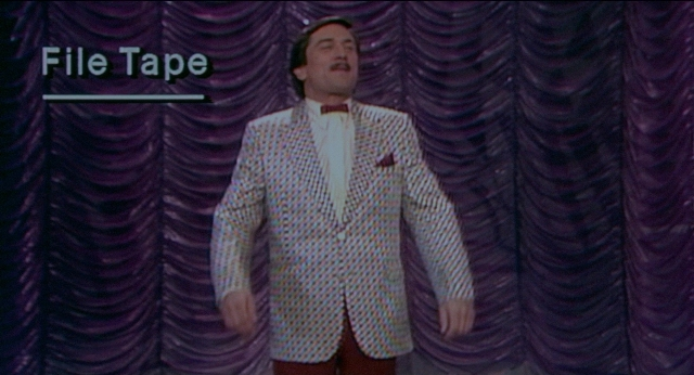 Wide shot frame from The King of Comedy — standing, tie, face