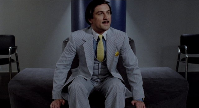Wide shot frame from The King of Comedy — sitting, room, suit
