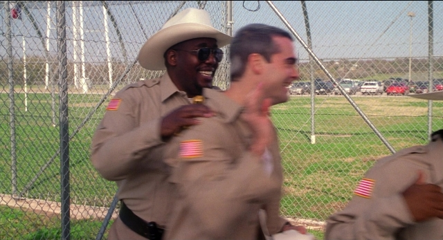 Wide shot frame from The New Guy — standing, hat, hand