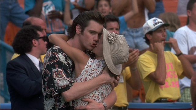 Wide shot frame from Ace Ventura: Pet Detective — standing, kiss, hat