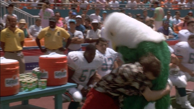 Wide shot frame from Ace Ventura: Pet Detective — standing, table, shirt