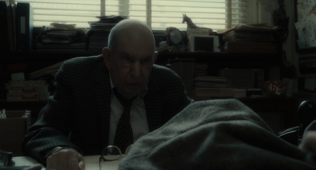 Wide shot frame from Inside Llewyn Davis — sitting, book, suit