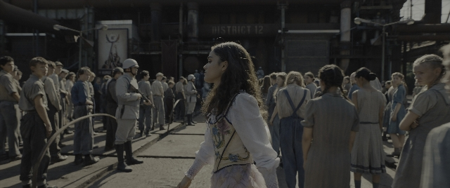 Wide shot frame from The Hunger Games: The Ballad of Songbirds & Snakes — standing, street, face