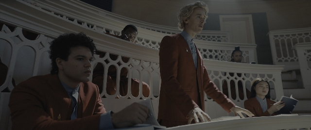 Wide shot frame from The Hunger Games: The Ballad of Songbirds & Snakes — sitting, book, standing