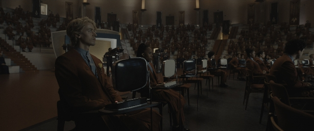 Wide shot frame from The Hunger Games: The Ballad of Songbirds & Snakes — sitting, room, suit