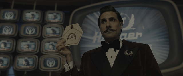 Medium shot frame from The Hunger Games: The Ballad of Songbirds & Snakes — standing, suit, mustache