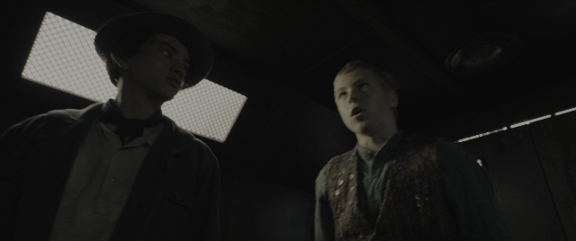 Wide shot frame from The Hunger Games: The Ballad of Songbirds & Snakes — standing, room, hat