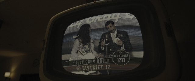 Wide shot frame from The Hunger Games: The Ballad of Songbirds & Snakes — sitting, dialogue, suit