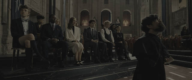 Wide shot frame from The Hunger Games: The Ballad of Songbirds & Snakes — sitting, book, standing