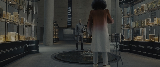 Wide shot frame from The Hunger Games: The Ballad of Songbirds & Snakes — standing, room, coat