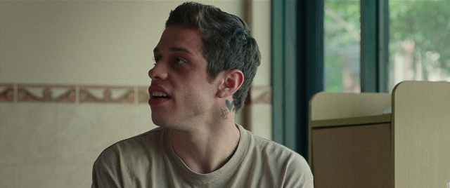 Wide shot frame from The King of Staten Island — sitting, room, shirt