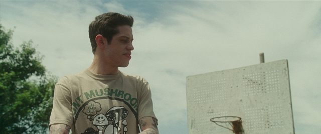 Wide shot frame from The King of Staten Island — standing, shirt, face