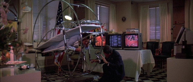 Frame from The Adventures of Buckaroo Banzai Across the 8th Dimension — standing, room, table