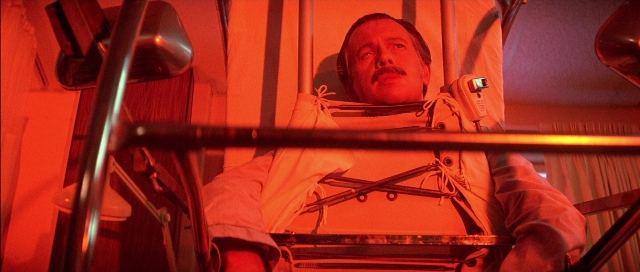 Wide shot frame from The Adventures of Buckaroo Banzai Across the 8th Dimension — sitting, bed, mustache