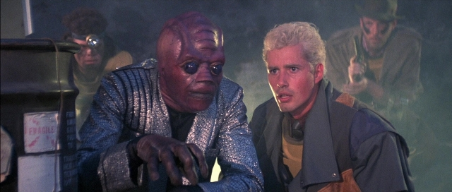 Wide shot frame from The Adventures of Buckaroo Banzai Across the 8th Dimension — sitting, room, face