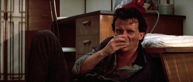 Wide shot frame from The Adventures of Buckaroo Banzai Across the 8th Dimension — sitting, bed, door