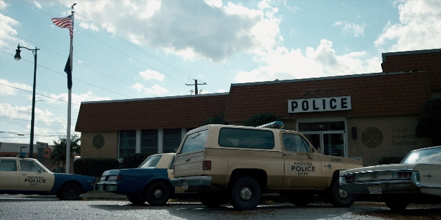 Wide shot frame from Stranger Things — street, flag, car