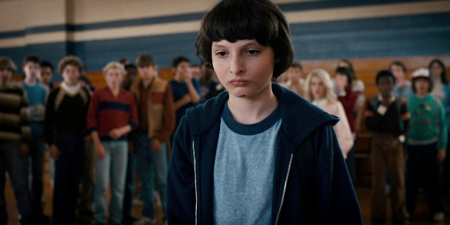 Medium shot frame from Stranger Things — standing, room, shirt