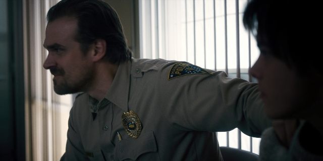 Wide shot frame from Stranger Things — sitting, uniform, shirt