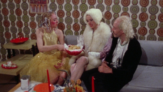 Wide shot frame from Female Trouble — sitting, plate, room