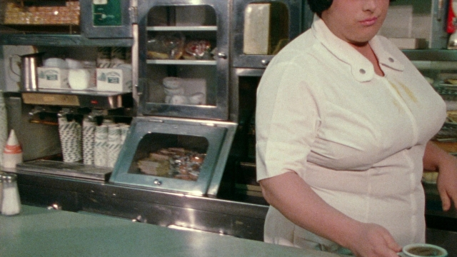 Wide shot frame from Female Trouble — standing, door, hat