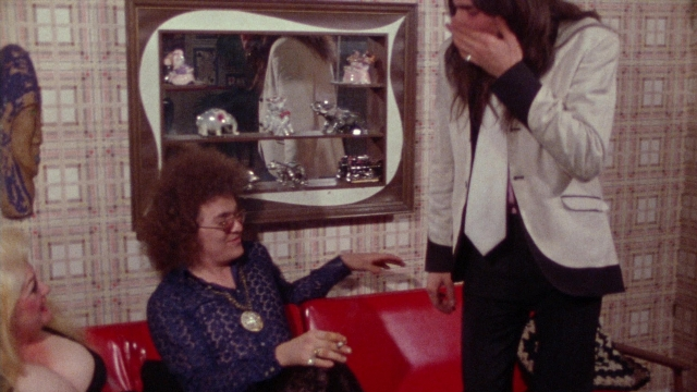 Wide shot frame from Female Trouble — sitting, standing, room