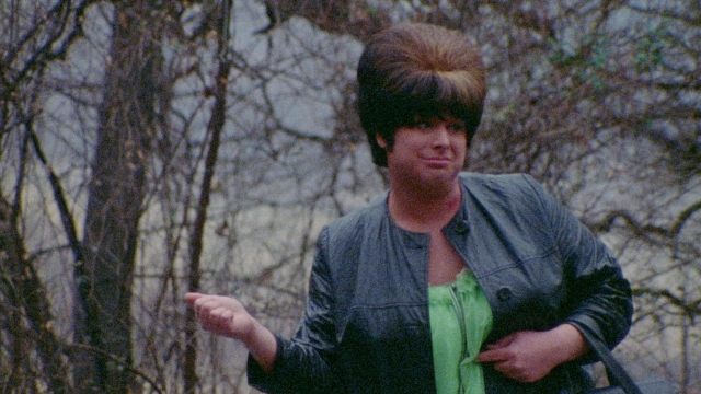 Wide shot frame from Female Trouble — standing, hand, jacket