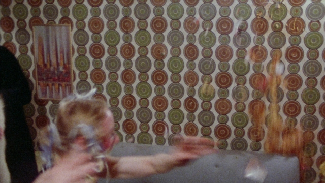 Medium shot frame from Female Trouble — room, hand, smoke