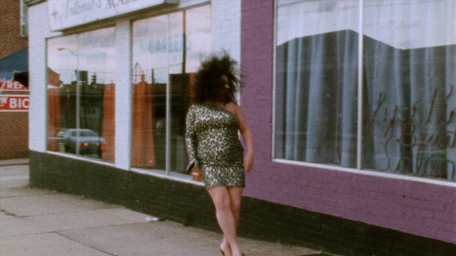 Wide shot frame from Female Trouble — walking, street, dress